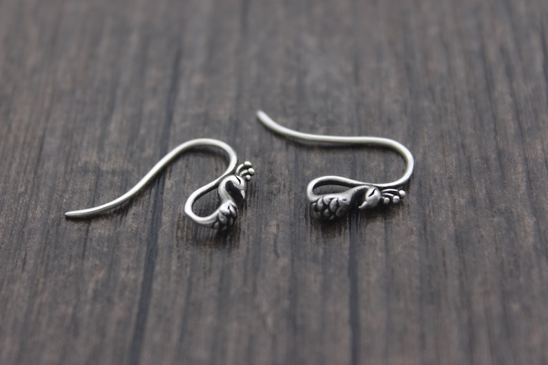 May include: A pair of silver peacock-shaped earrings with a hook fastening.