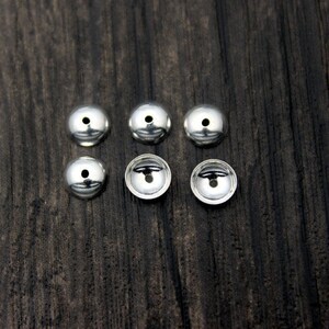 May include: Six silver metal beads with a small hole in the center of each bead.