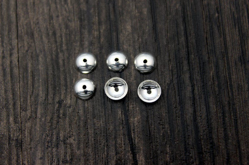 May include: Six silver metal beads with a small hole in the center of each bead.