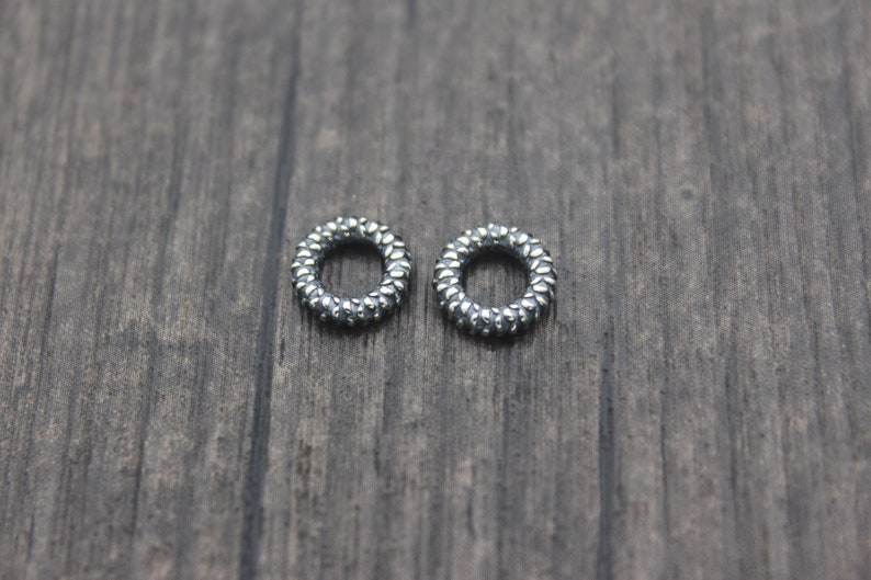 May include: Two silver rings with a textured surface. The rings are round and have a small opening in the center.