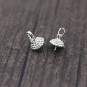 May include: Two silver-toned pearl caps with a small clear rhinestone accent. The caps have a textured, domed design and a loop for attaching a string or chain.