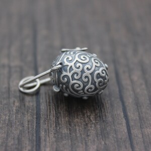 May include: A silver charm in the shape of a small, ornate egg with a swirl design. The charm has a small loop at the top for attaching to a necklace or bracelet.