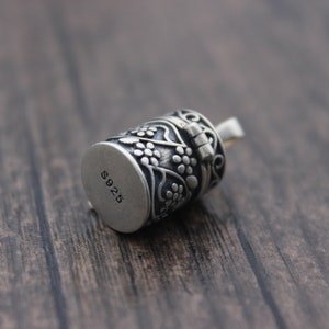 May include: Silver charm with a floral design and a hinged lid. The charm is marked with "S925" on the bottom.