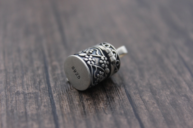 May include: Silver charm with a floral design and a hinged lid. The charm is marked with "S925" on the bottom.