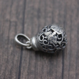 Puede incluir: Pendiente de plata con un dise&ntilde;o floral detallado, que incluye una flor de loto y un intrincado trabajo de volutas. El pendiente es hueco y tiene un bucle para sujetarlo a una cadena.