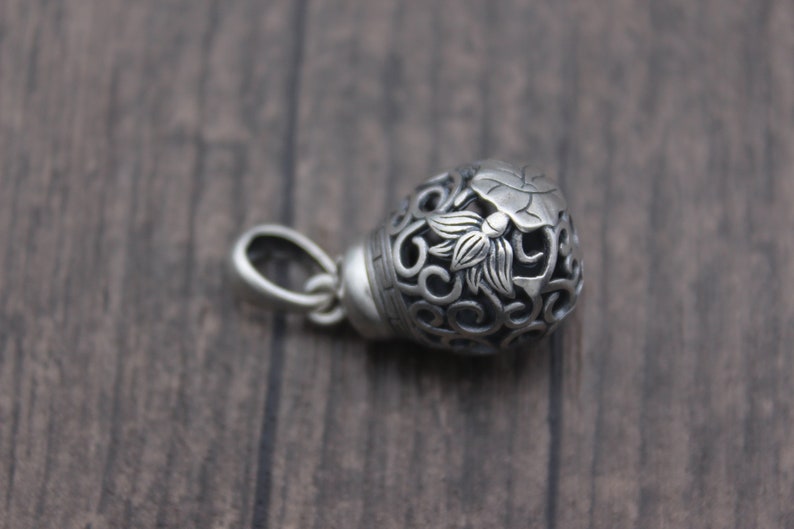 Puede incluir: Pendiente de plata con un dise&ntilde;o floral detallado, que incluye una flor de loto y un intrincado trabajo de volutas. El pendiente es hueco y tiene un bucle para sujetarlo a una cadena.