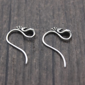 May include: A pair of silver earrings featuring a bird design. The earrings are long and curved, with the bird design at the top.