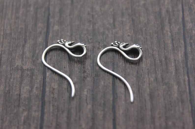 May include: A pair of silver earrings featuring a bird design. The earrings are long and curved, with the bird design at the top.