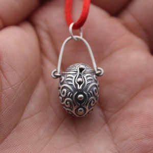May include: A silver pendant necklace with a small, ornate, hinged box charm. The box is decorated with a swirling, abstract pattern.