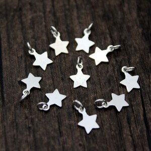 May include: A collection of ten silver star-shaped charms, arranged in a circle on a wooden surface.
