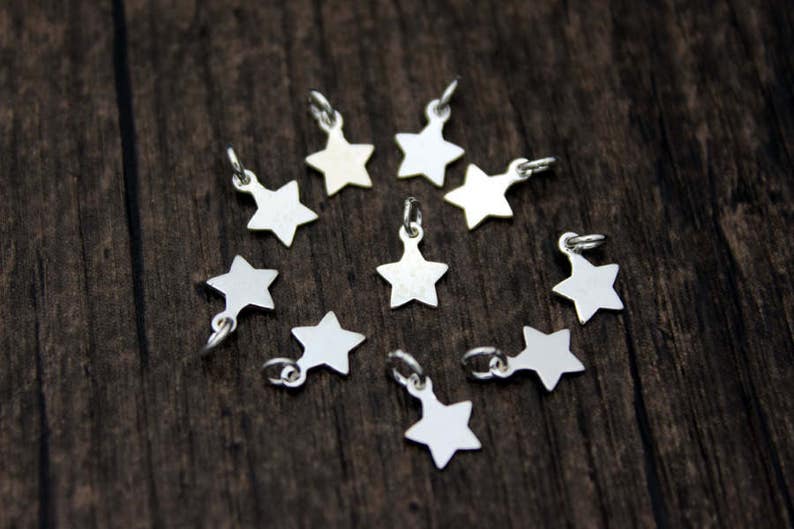May include: A collection of ten silver star-shaped charms, arranged in a circle on a wooden surface.