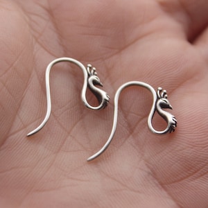 May include: A pair of silver peacock-shaped earrings with a hook fastening.