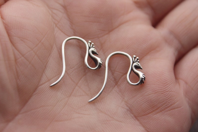 May include: A pair of silver peacock-shaped earrings with a hook fastening.