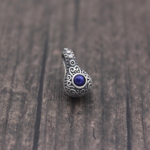 May include: A silver pendant with an intricate design and a blue gemstone in the centre.