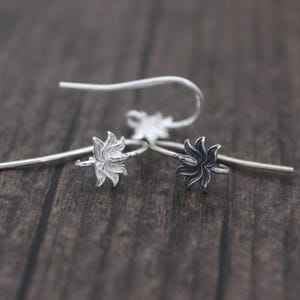 以下が含まれることがあります： 蓮の花のデザインが施された銀製のイヤリング金具が2つ。1つは銀色、もう1つは黒色です。