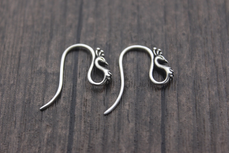 May include: A pair of silver peacock-shaped earrings with a hook fastening.