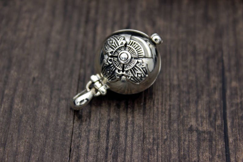 May include: A silver charm with an intricate floral design. The charm is round and has a small loop at the top for attaching to a necklace or bracelet.