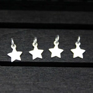 May include: Four silver star-shaped charms with jump rings. The charms are arranged in a row on a dark wooden surface.