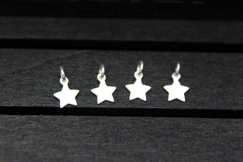 May include: Four silver star-shaped charms with jump rings. The charms are arranged in a row on a dark wooden surface.