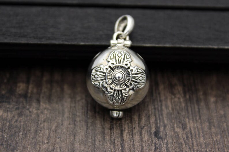 May include: A silver pendant in the shape of a sphere with intricate floral designs. The pendant has a loop at the top for attaching to a chain.