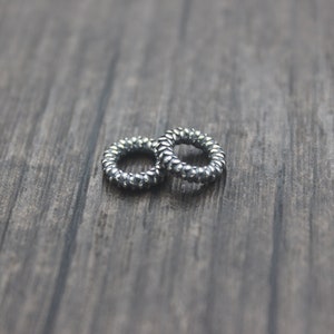 May include: Two silver hair ties, made of a coiled metal, are lying on a wooden surface.