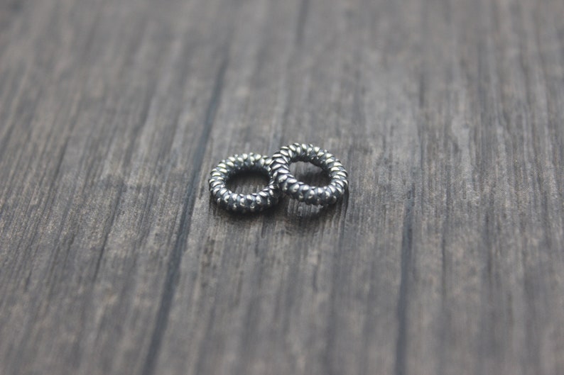 May include: Two silver hair ties, made of a coiled metal, are lying on a wooden surface.
