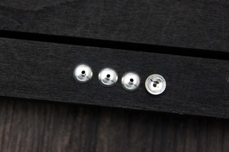 May include: Five silver metal beads with a hole in the center, arranged in a row on a dark wooden surface.