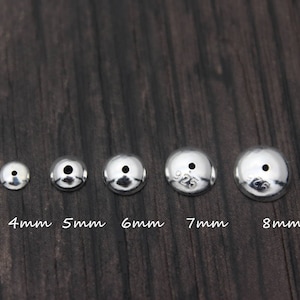 May include: Five silver-toned metal bead caps in different sizes, ranging from 4mm to 8mm. The bead caps are round and have a small hole in the center. The bead caps are arranged in a row from smallest to largest.