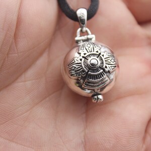 May include: A silver pendant necklace with a round, ornate charm. The charm has a detailed design with a central circle and radiating lines.