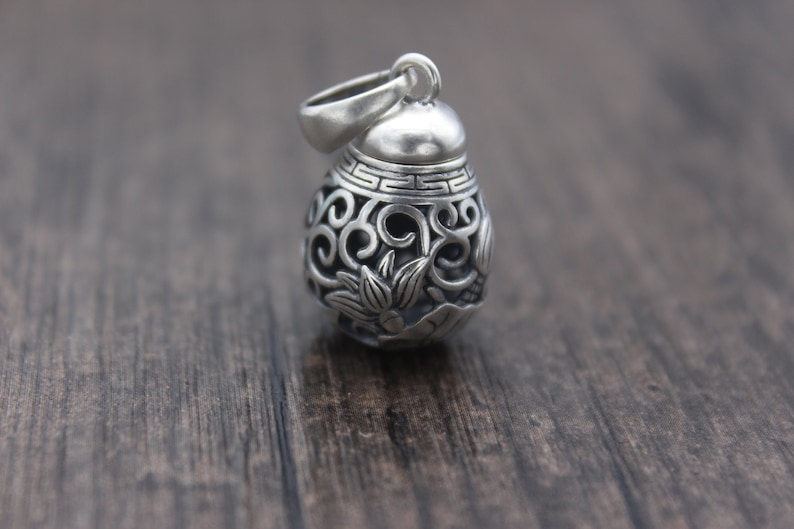 Puede incluir: Un colgante de plata con un intrincado dise&ntilde;o floral. El colgante es redondo y tiene una peque&ntilde;a abertura en la parte superior para una cadena.