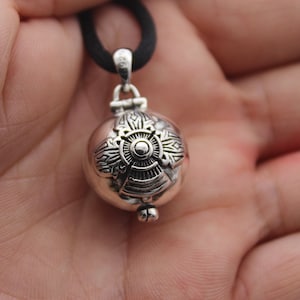 May include: Silver pendant necklace with a round, ornate charm. The charm has a detailed design with a central circle and radiating lines.