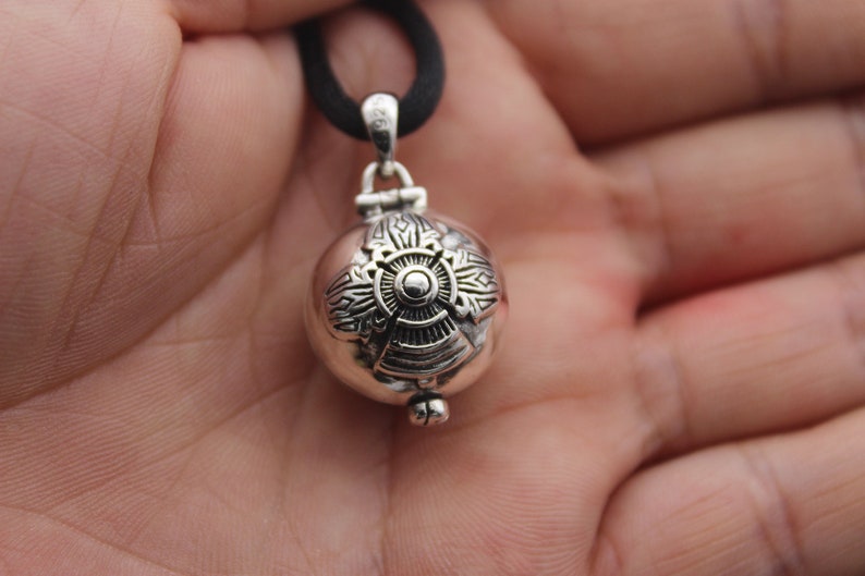 May include: Silver pendant necklace with a round, ornate charm. The charm has a detailed design with a central circle and radiating lines.