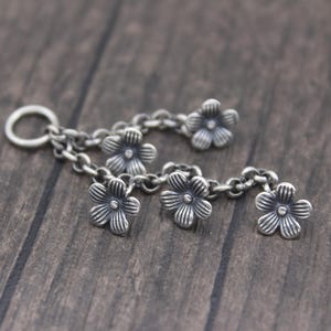 May include: A silver charm bracelet with a chain and five flower-shaped charms. The charms are detailed with textured petals and a small center circle.