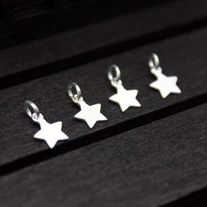 May include: Five silver star-shaped charms with jump rings. The charms are arranged in a row on a black wooden surface.