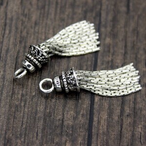 Peut inclure: Deux breloques en argent en forme de glands avec un design d&eacute;taill&eacute; et orn&eacute;. Les glands sont faits d'un mat&eacute;riau en cha&icirc;ne et ont une boucle en argent pour &ecirc;tre attach&eacute;s &agrave; un bracelet ou un collier.