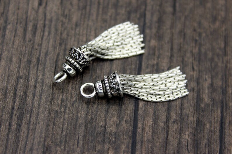 Peut inclure: Deux breloques en argent en forme de glands avec un design d&eacute;taill&eacute; et orn&eacute;. Les glands sont faits d'un mat&eacute;riau en cha&icirc;ne et ont une boucle en argent pour &ecirc;tre attach&eacute;s &agrave; un bracelet ou un collier.