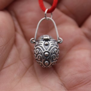 May include: A silver pendant necklace with a detailed, ornate, oval-shaped locket. The locket has a hinged lid and a delicate chain.