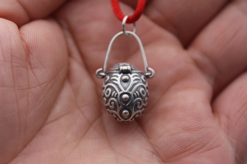 May include: A silver pendant necklace with a detailed, ornate, oval-shaped locket. The locket has a hinged lid and a delicate chain.