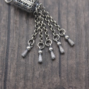 May include: Silver charm with a detailed filigree design and multiple dangling chains with small tassel-like ends.
