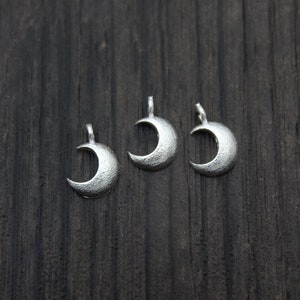 May include: Three silver crescent moon charms on a dark wood background.