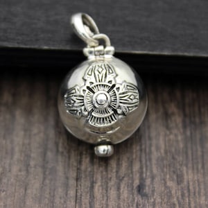 May include: A silver charm pendant with an intricate design. The pendant is round and has a small loop at the top for attaching to a chain.