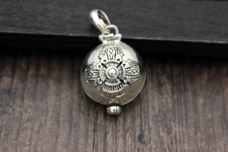 May include: A silver charm pendant with an intricate design. The pendant is round and has a small loop at the top for attaching to a chain.