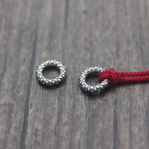 May include: Two silver metal rings with a textured surface. One ring is threaded with a red cord.