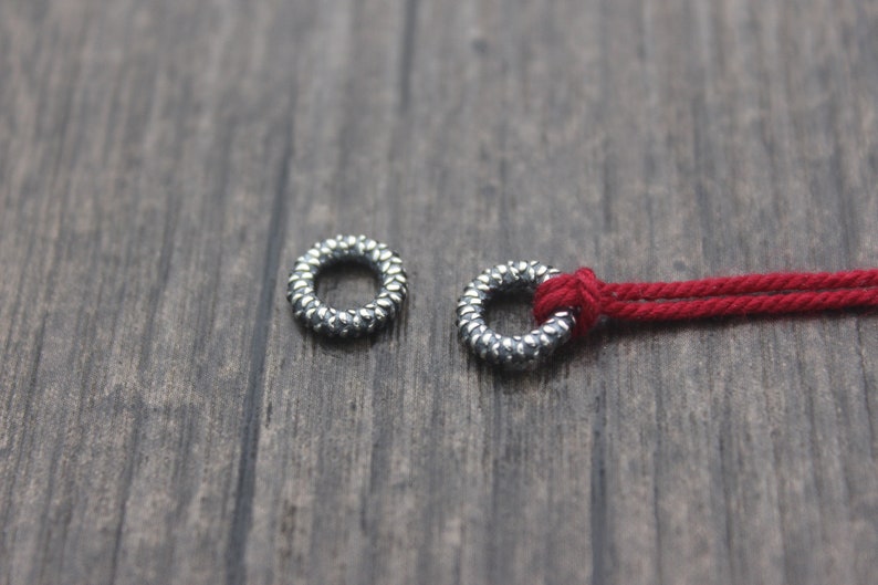 May include: Two silver metal rings with a textured surface. One ring is threaded with a red cord.