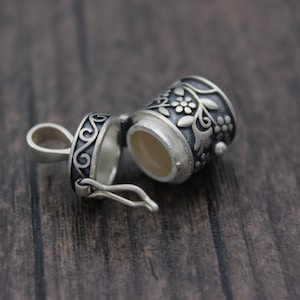 May include: A silver charm with a floral design, the charm is open and has a small compartment inside.