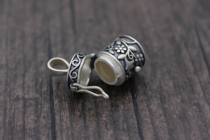 May include: A silver charm with a floral design, the charm is open and has a small compartment inside.
