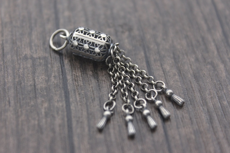 May include: A silver charm with a detailed filigree design and a dangling chain with five tassels.