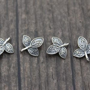 May include: Four silver leaf charms with intricate details. Each charm features three leaves with a delicate design.