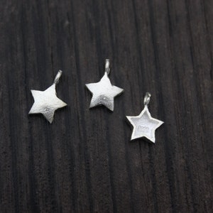May include: Three silver star-shaped charms with a loop at the top for attaching to jewelry or other crafts.