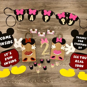 May include: A set of Mickey Mouse themed party decorations, including a banner with the words "Happy", two Mickey Mouse head cutouts with the text "Come Inside" and "Thanks for Stopping By", two brown paper bags with Mickey Mouse ears and bows, and a number two with glitter.